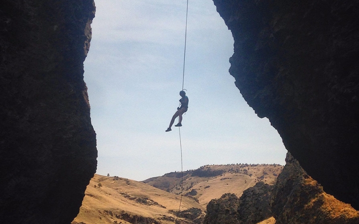 Wearing safety gear is suspended by ropes, midair, between two rock walls. 